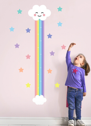 ملصق قياس الطول سحابة قوس قزح على جدار وردي مع فتاة صغيرة تقف بجانبه